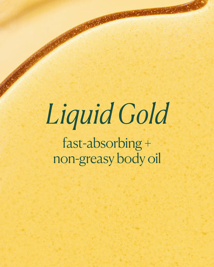 A close-up of a golden yellow liquid body oil with the text 'Liquid Gold' and 'fast-absorbing + non-greasy body oil' printed in dark green on the surface.