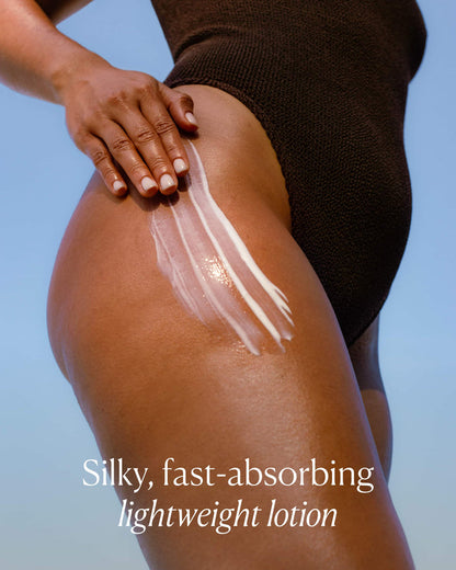 Person applying lotion to their leg with a clear blue sky background
