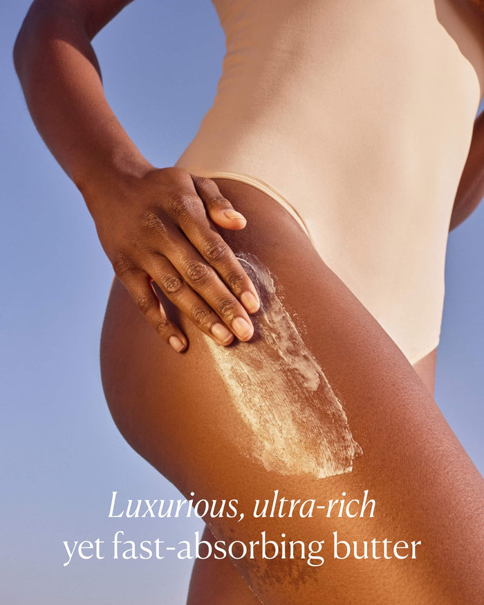 Person applying luxurious ultra-rich butter to their skin with a clear blue sky background